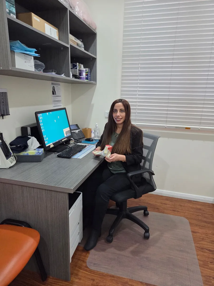 Madleen Farhan at her desk in the Harrington Park clinic, holding a foot anatomy model